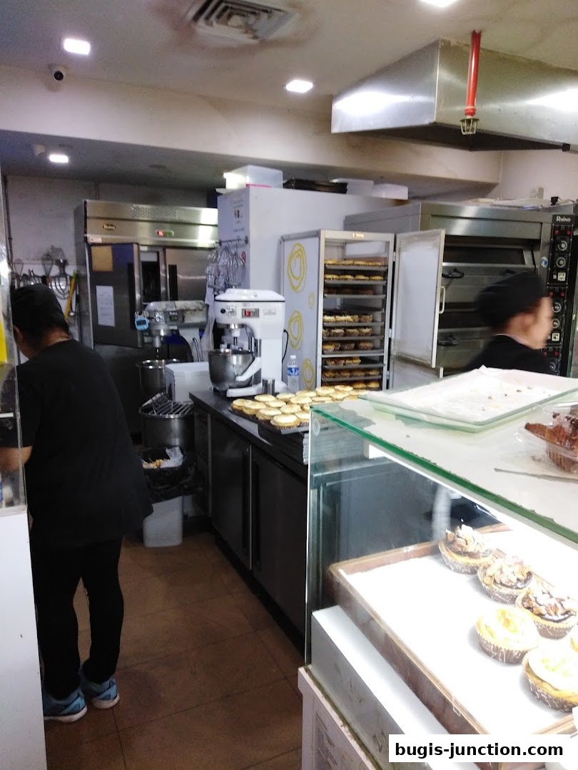 Interior view of a bakery with staff, ovens, and display cases filled with pastries.