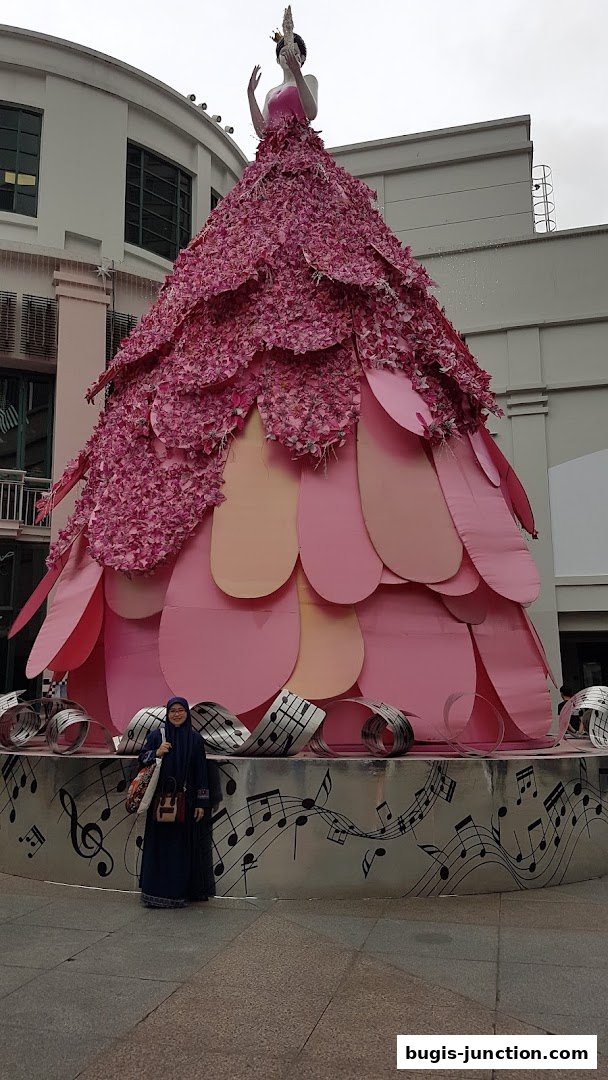A person stands in front of a large, pink, floral-themed display with musical notes.