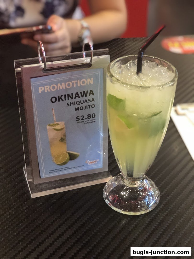 A promotional sign for Okinawa Shiquasa Mojito next to a refreshing drink.