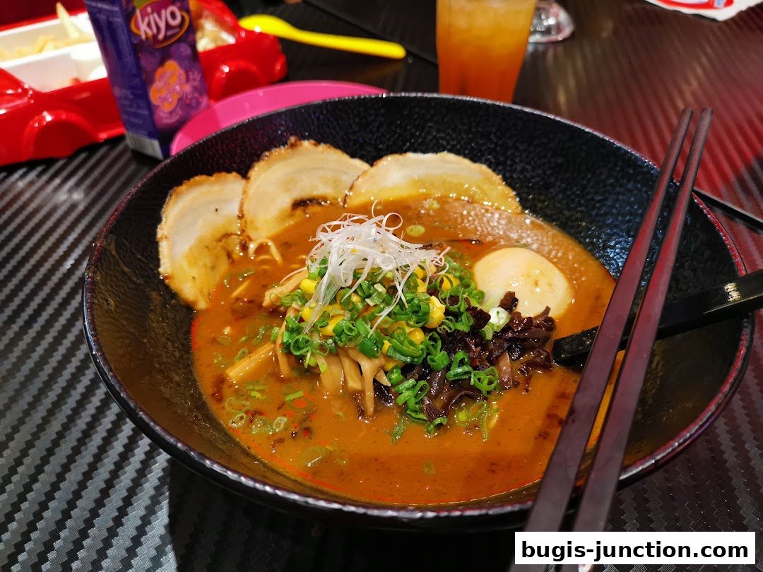 A steaming bowl of curry ramen with pork slices, egg, and vegetables, served with chopsticks.