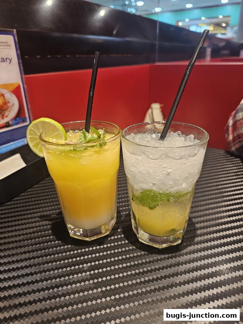 Two refreshing drinks, one yellow and one clear with ice and mint, are displayed on a textured table.