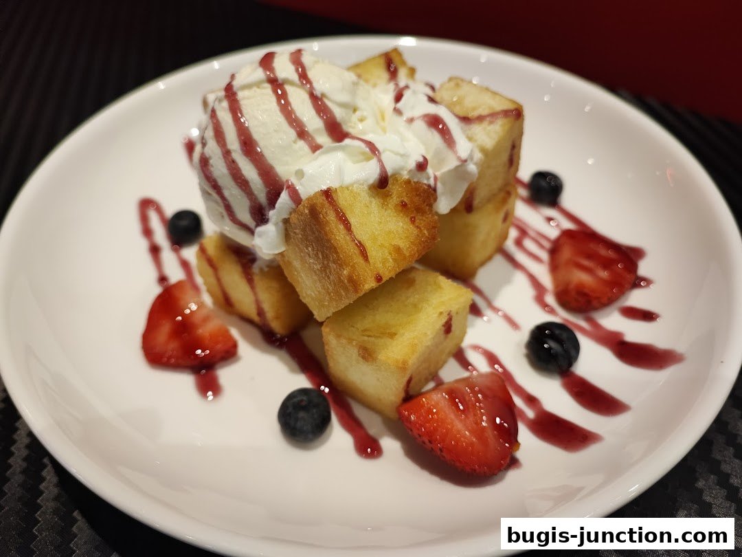 A delicious dessert featuring toast cubes, ice cream, whipped cream, strawberries, and blueberries.