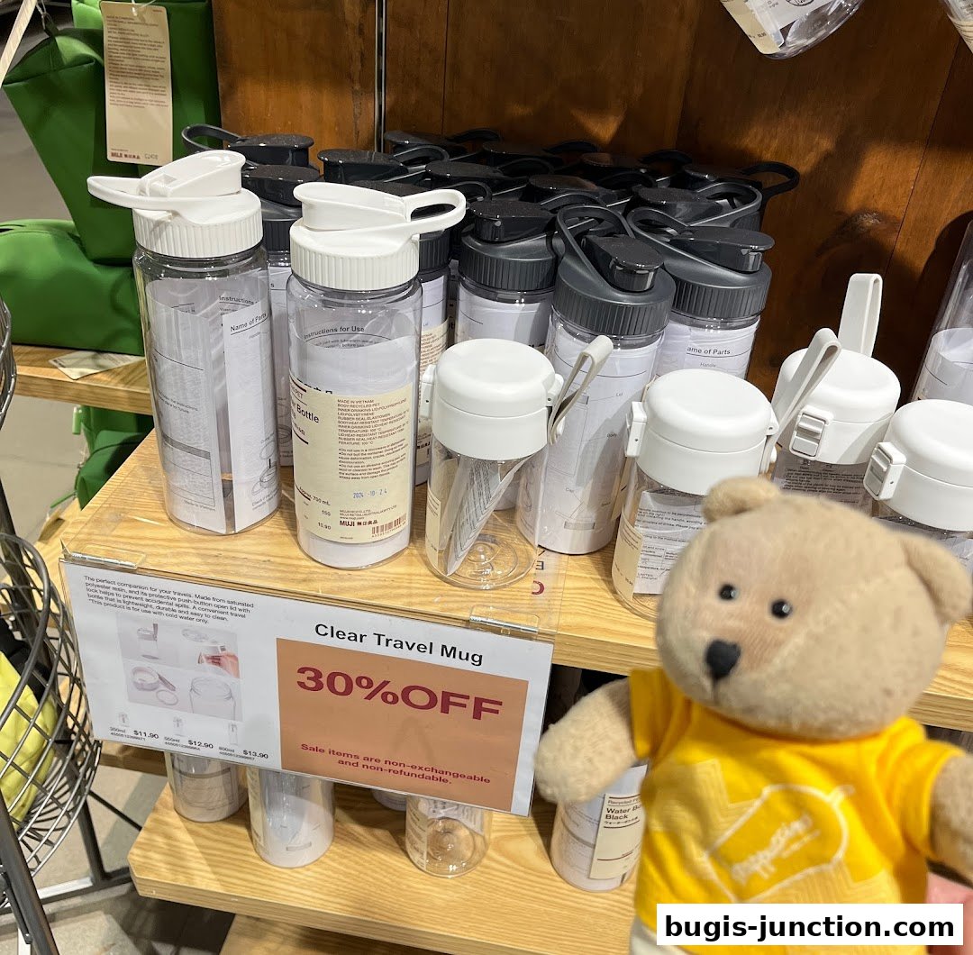 A display of clear travel mugs with a 30% off sale sign and a teddy bear.
