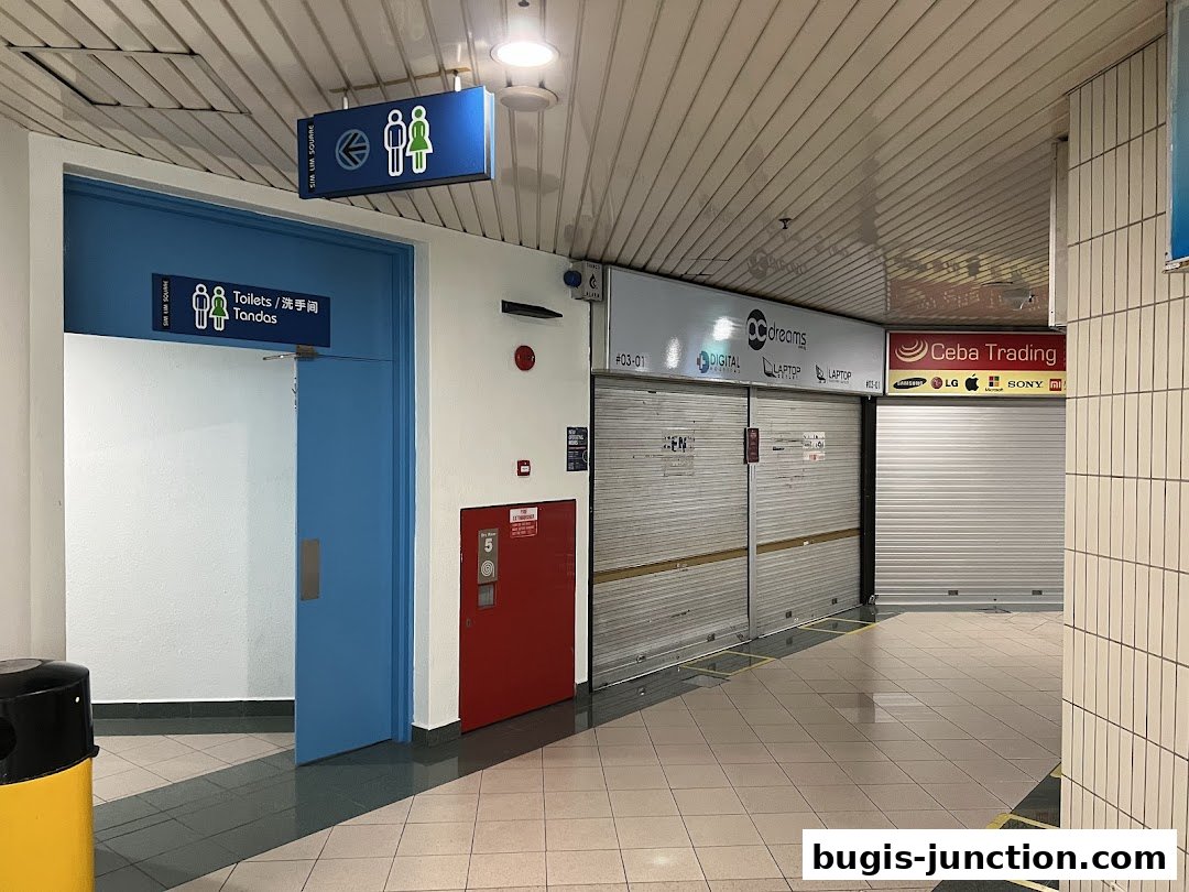 A hallway with closed shop shutters and a blue door labeled 'Toilets'.