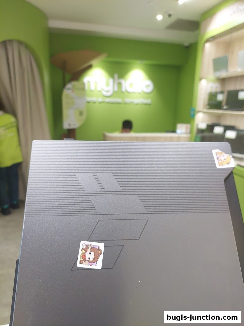 A laptop with stickers in front of a brightly lit store with the 'myhalo' logo.