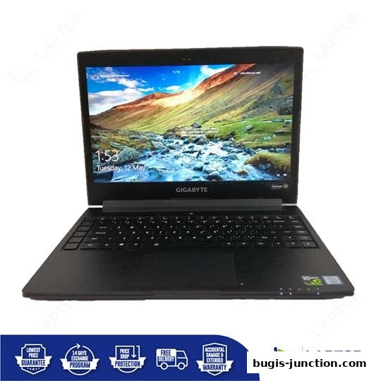 A black Gigabyte laptop is displayed with its screen showing a scenic landscape and the time.