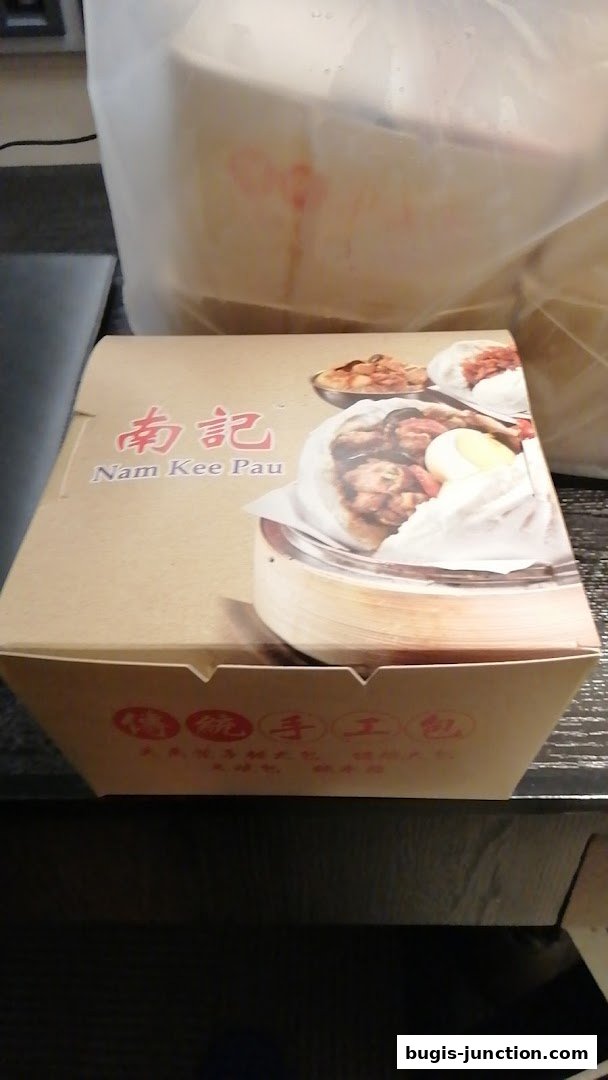 A takeout box from Nam Kee Pau featuring steamed buns and other savory dishes.