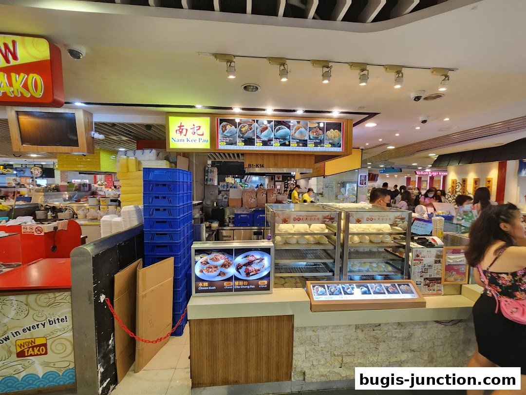 The Nam Kee Pau shop front with steamed buns displayed and a menu board above.
