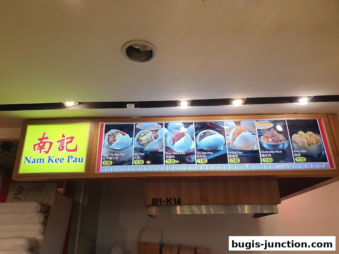 A menu board for Nam Kee Pau, showcasing various steamed buns and dim sum items with prices.