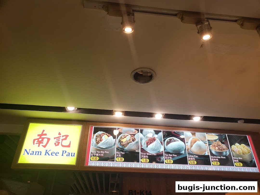 A menu board for Nam Kee Pau displaying various steamed buns and rice dishes with prices.