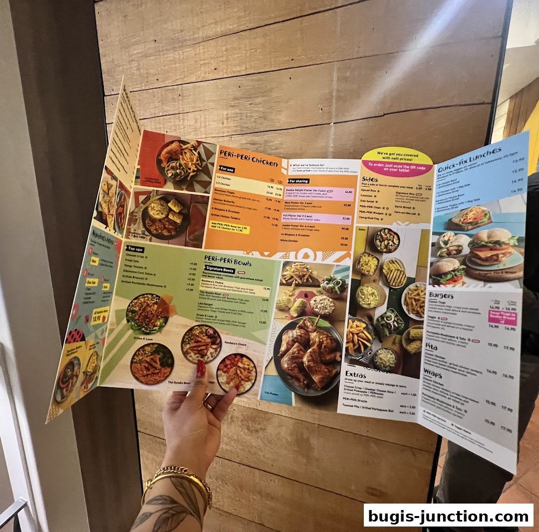 A person holds open a Nandos menu featuring PERi-PERi chicken, bowls, burgers, and sides.