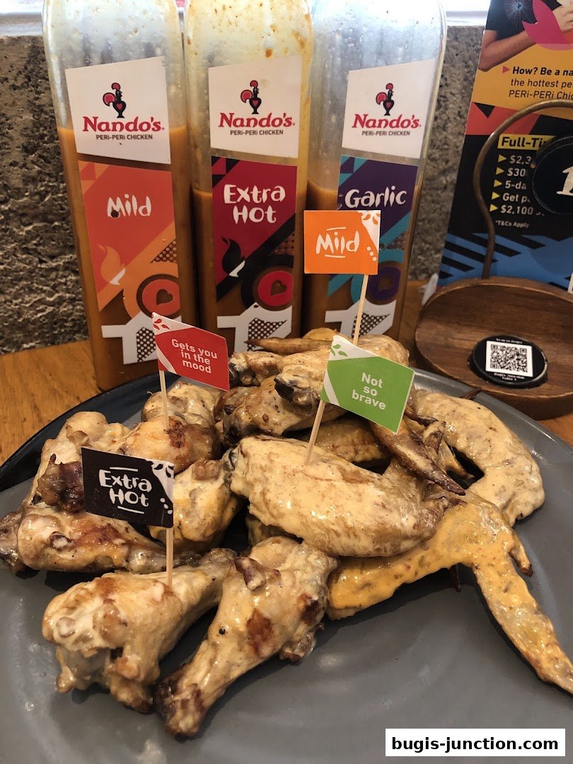A platter of Nando's peri-peri chicken wings with bottles of sauce and flavor flags.