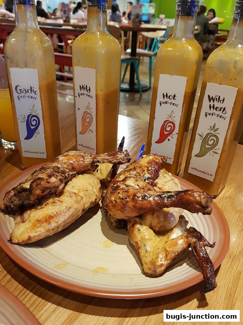 A plate of flame-grilled chicken with bottles of peri-peri sauce in the background.