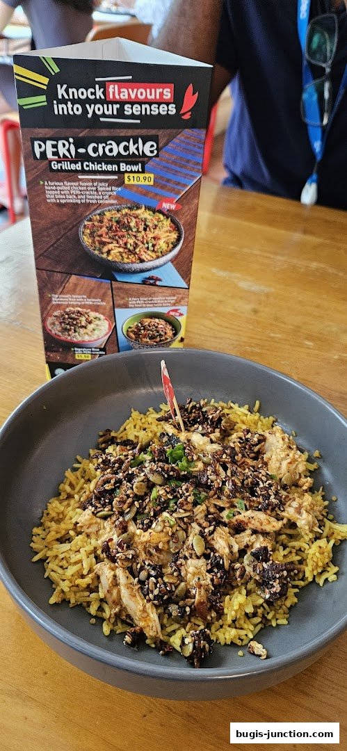 A bowl of PERi-crackle grilled chicken with rice and toppings, next to a menu stand.