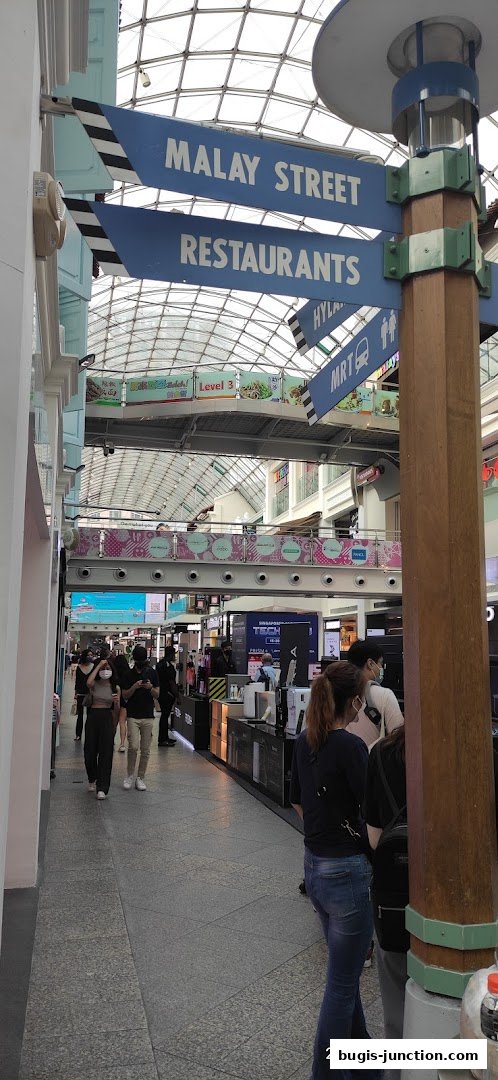 A busy indoor walkway with directional signs and shops on the side.