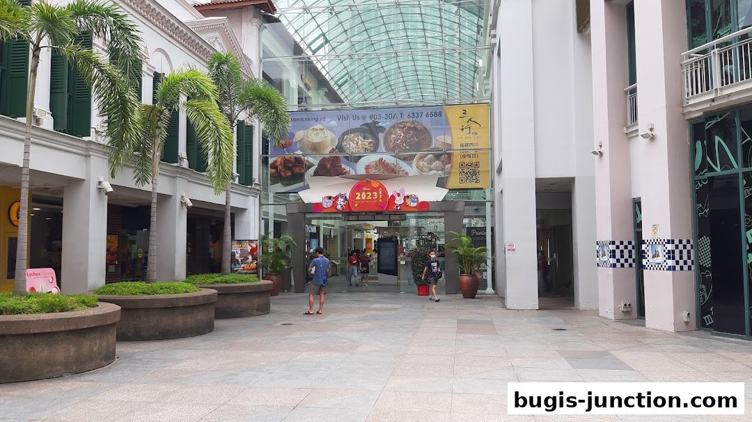 The entrance to a shopping mall with palm trees and a large banner advertising food.