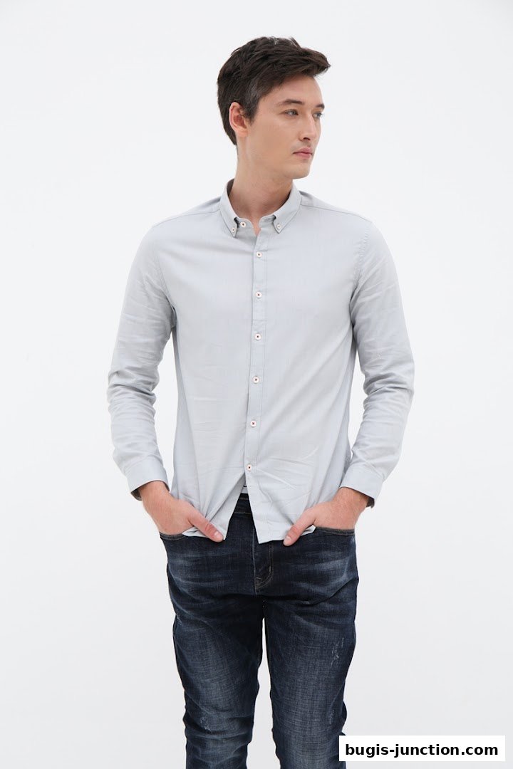 A man wearing a light blue button-down shirt and dark wash jeans with his hands in his pockets.