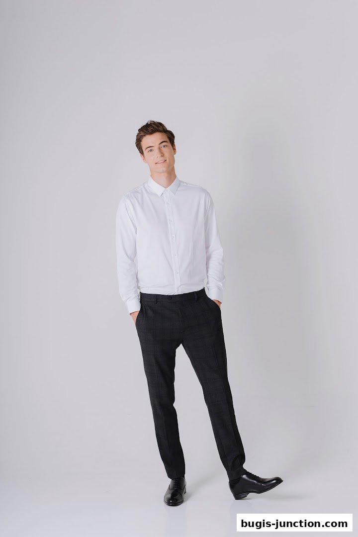 A smiling man in a white dress shirt and checkered trousers poses with hands in pockets.