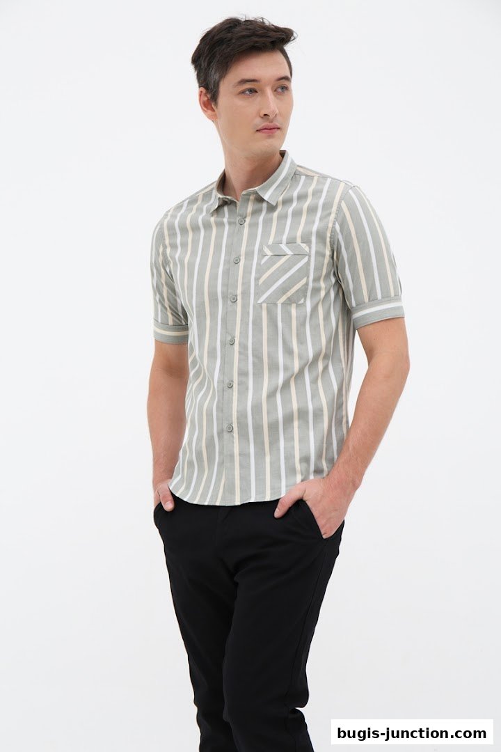 A man wearing a striped short-sleeved shirt and black pants with his hands in his pockets.