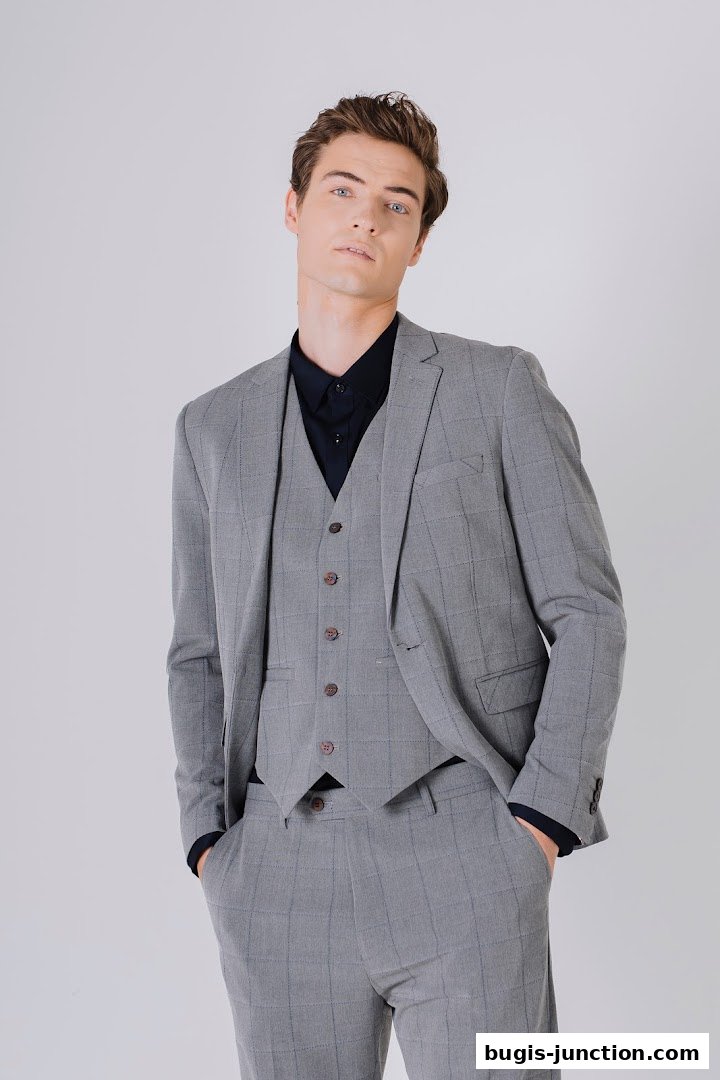 A man models a grey checkered suit with a navy shirt and vest.