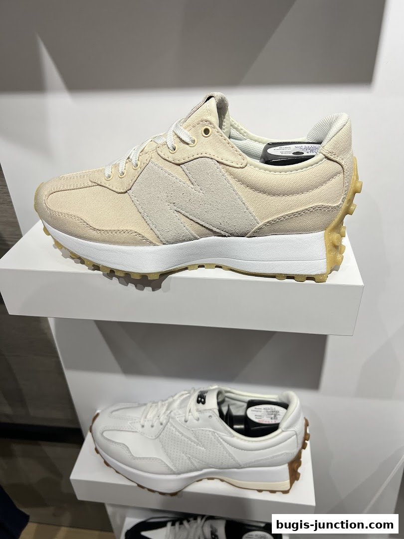 Two pairs of New Balance sneakers displayed on white shelves in a retail store.