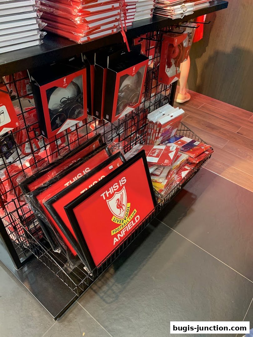 Liverpool FC merchandise including framed signs, headphones, and other accessories displayed on shelves.