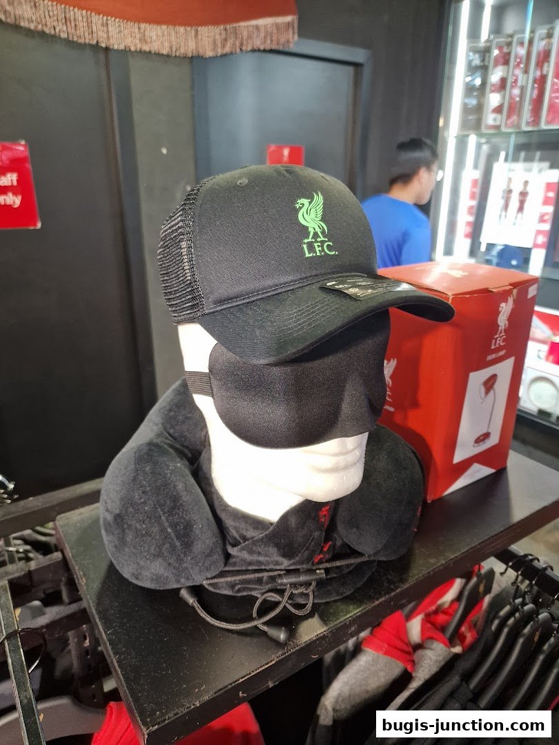 A Liverpool FC branded cap and travel pillow displayed on a shelf in a retail store.