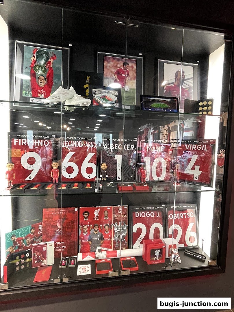 Display case filled with Liverpool FC memorabilia, including signed jerseys and player photos.