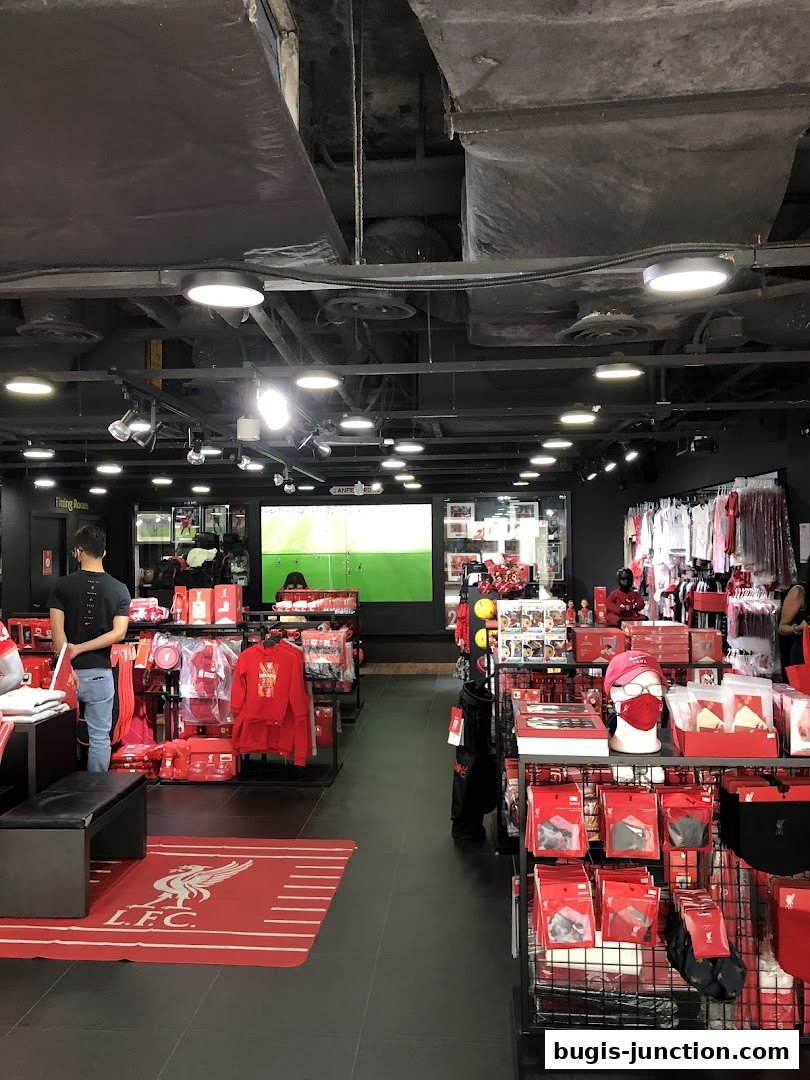 Interior of a Liverpool FC retail store showcasing merchandise and a large screen displaying a football match.
