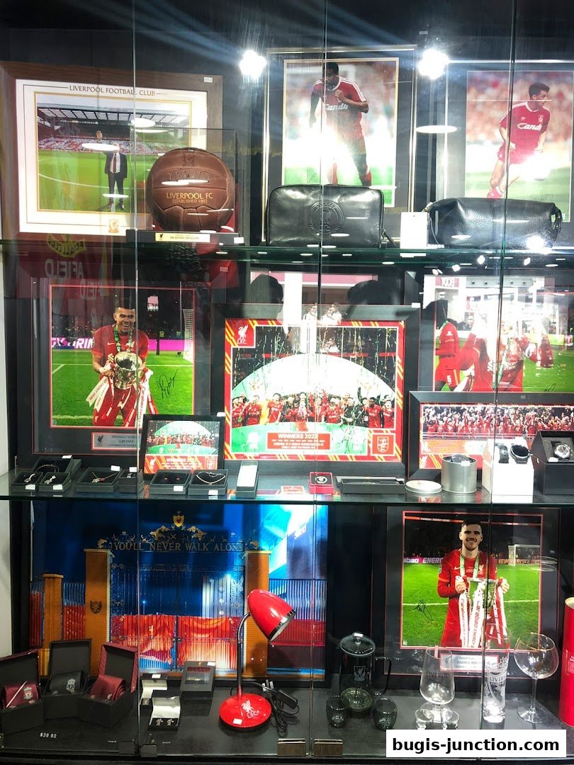 A display case filled with Liverpool FC memorabilia, including framed photos, footballs, and accessories.