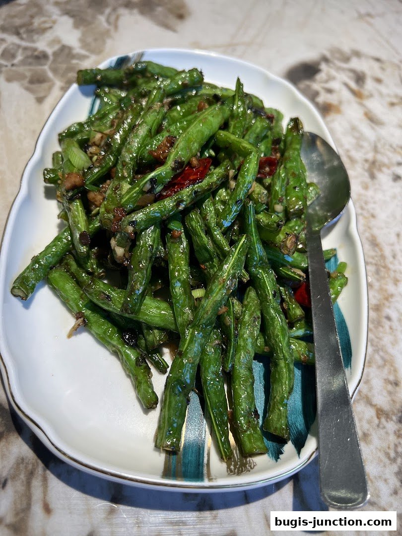 A plate of stir-fried green beans with chili and garlic, served with a spoon.