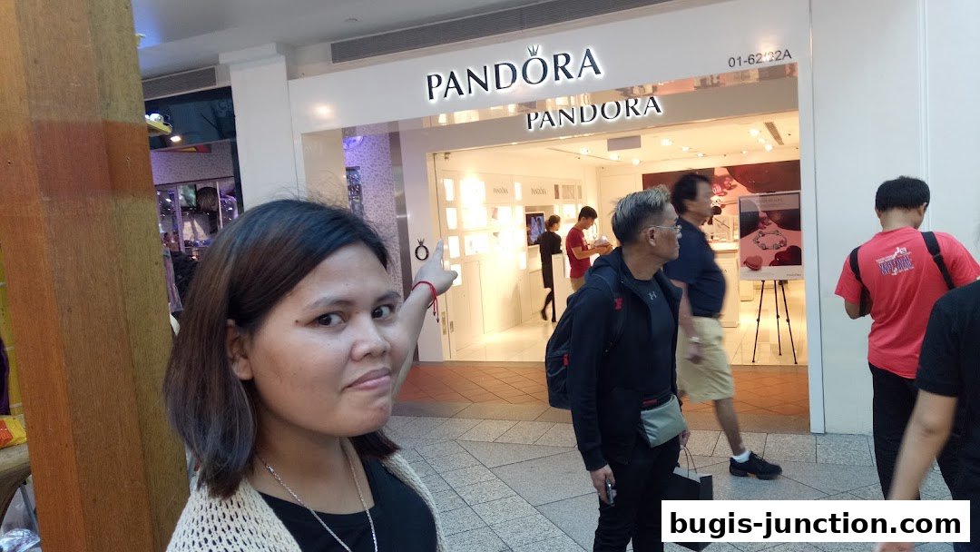 A woman points towards the Pandora store entrance, with shoppers inside and passing by.