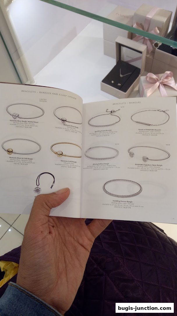A person is holding a Pandora catalog showcasing various bracelets and bangles.