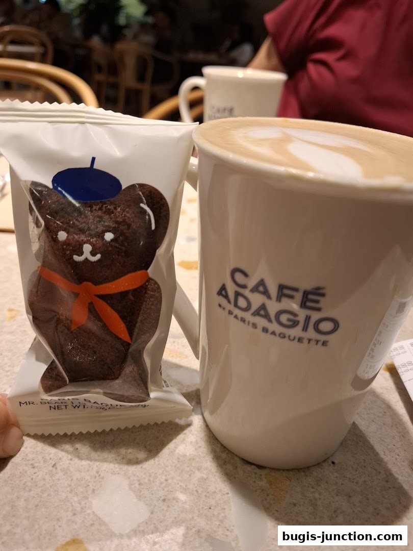 A packaged chocolate bear cookie and a latte with latte art from Cafe Adagio by Paris Baguette.