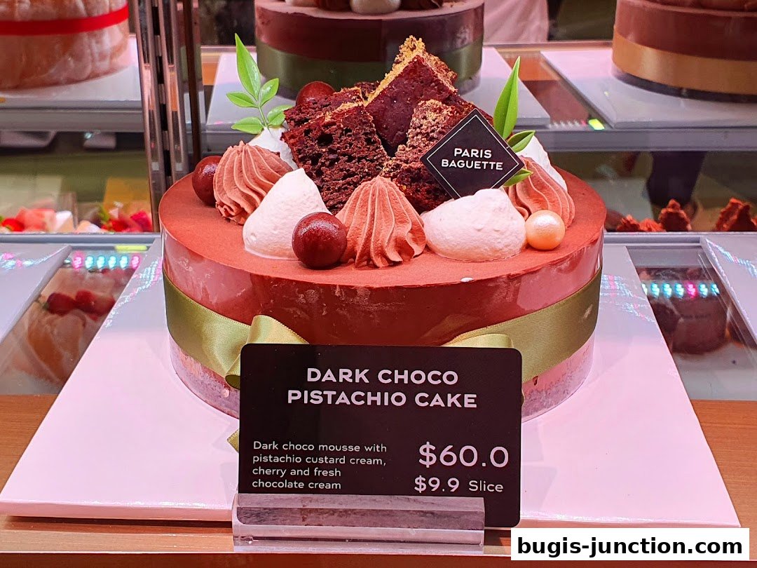 A beautifully decorated dark chocolate and pistachio cake with cream swirls and chocolate pieces.