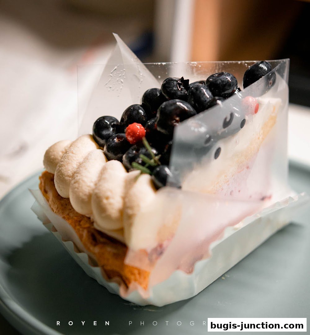 A close-up of a delicious blueberry tart with cream and a red berry.
