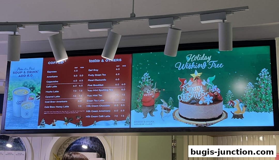 A digital menu board displaying coffee, tea, and holiday cake options with prices.