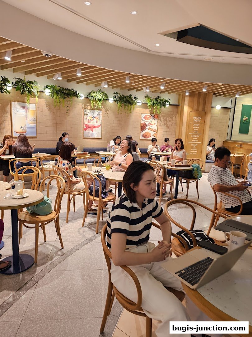 People enjoying coffee and pastries inside a bright, modern cafe with decorative plants.