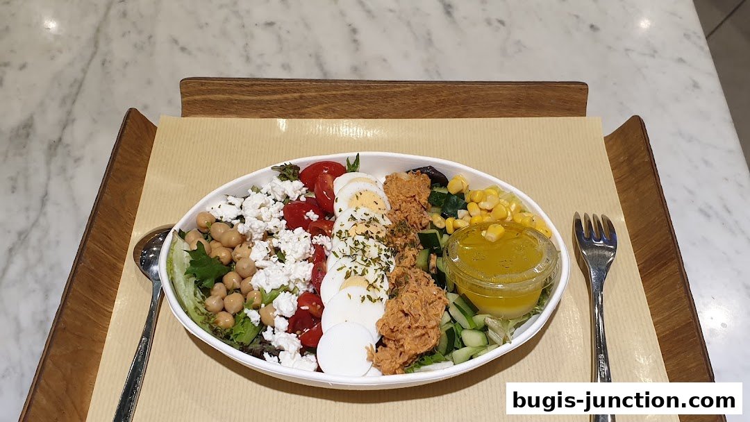 A vibrant salad with tuna, eggs, feta cheese, tomatoes, chickpeas, corn, and cucumber, served with dressing.