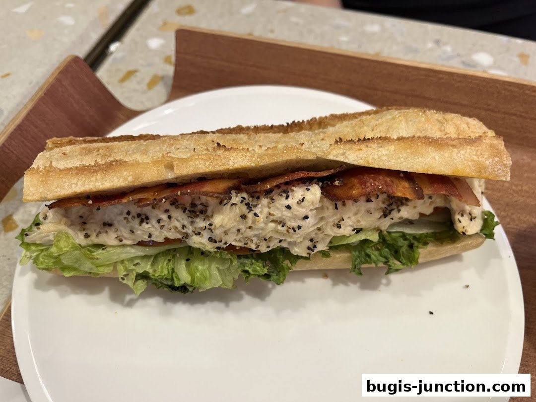 A delicious sandwich with bacon, chicken salad, lettuce, and tomato on a baguette.