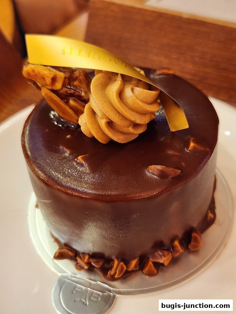 A decadent chocolate cake with caramel frosting and nuts, presented on a white plate.