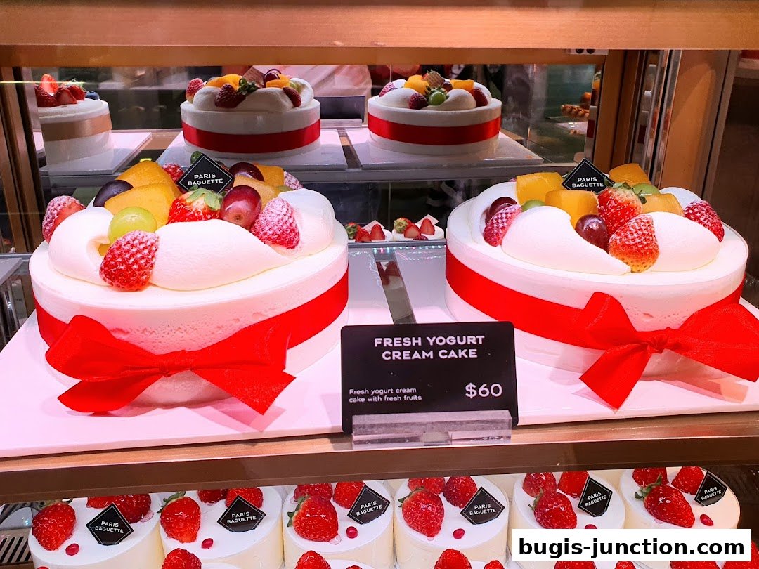 Two beautifully decorated cakes with fresh fruits and red ribbons on display.