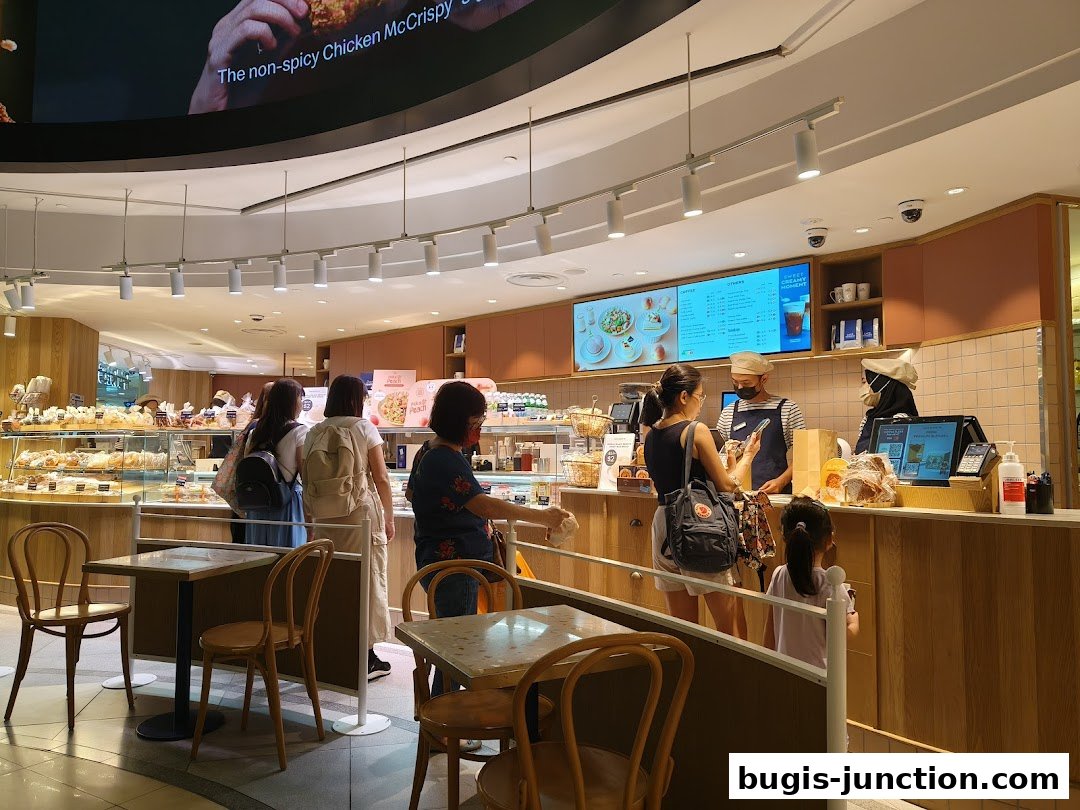 Customers ordering at the counter of a bright bakery with display cases of pastries.