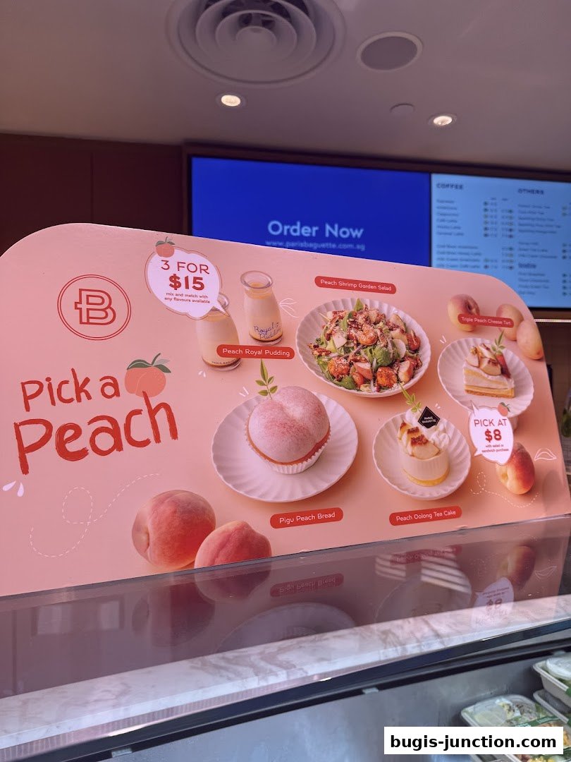 A display board showcasing peach-themed desserts and a salad from Paris Baguette.