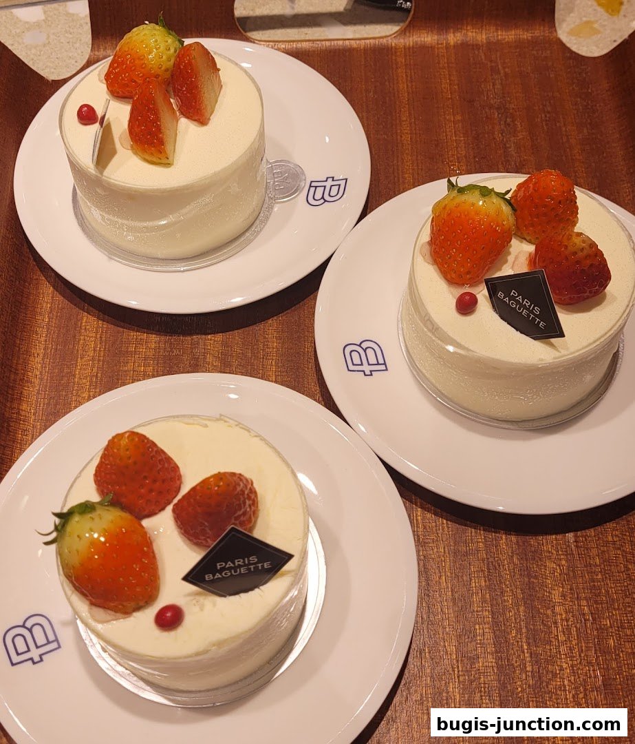 Three small white cakes topped with fresh strawberries and a red berry on white plates.