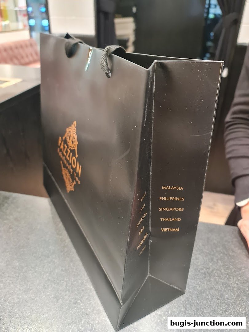 A black shopping bag with the PAZZION logo and a list of countries printed on its side.