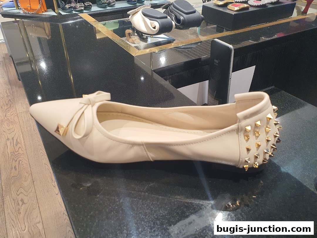 A close-up of a stylish beige flat shoe with a bow and gold studs on the heel.