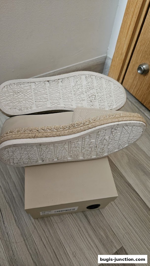 A pair of beige espadrille flats with a jute trim and patterned soles on a box.