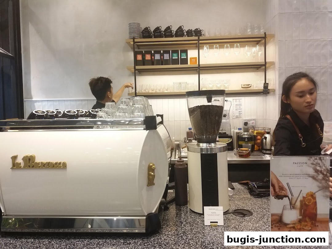 Baristas working behind a coffee machine with coffee beans and cups on shelves.