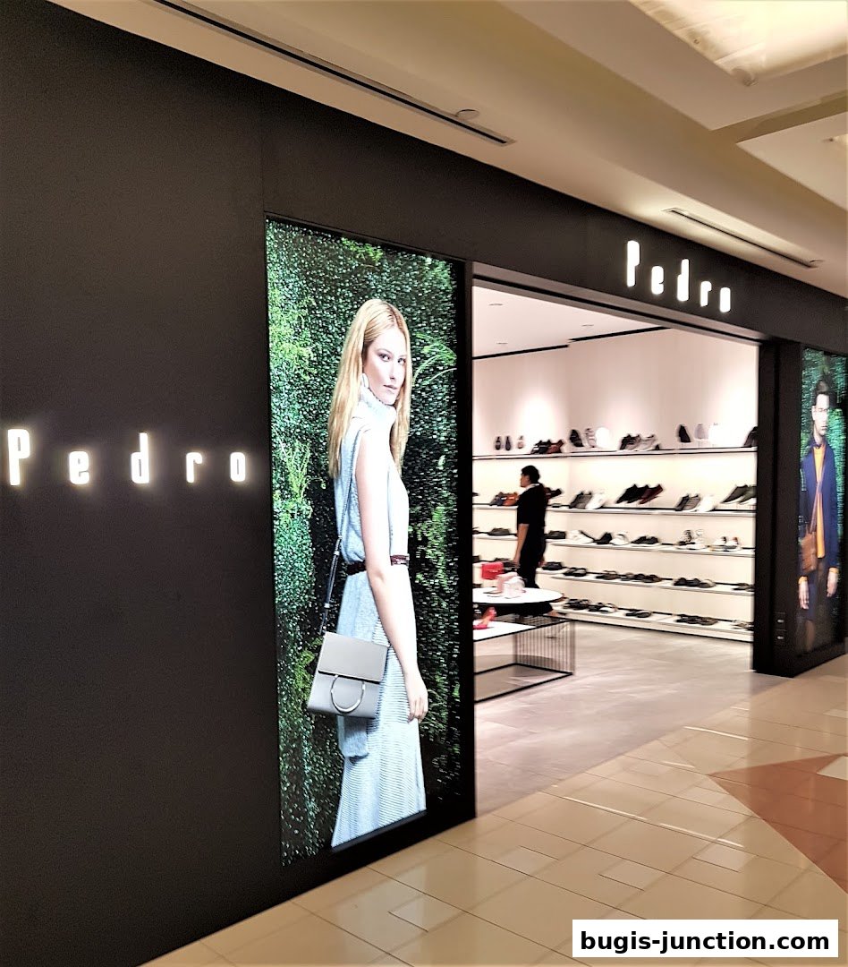 The Pedro shoe store entrance features a large display of a model with a handbag and shelves of shoes inside.